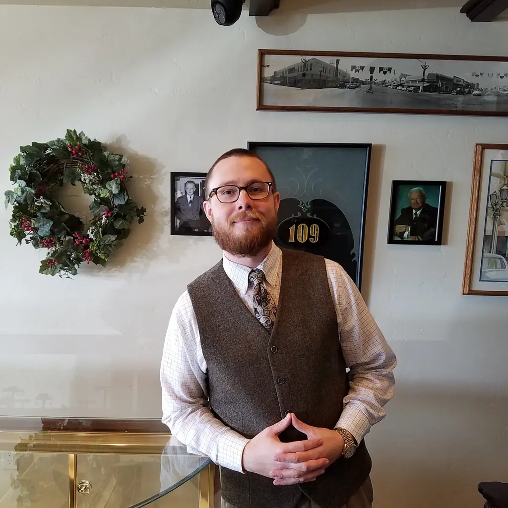 A staff member at the case, in front of the framed heritage photographs and the gold-leaf 109 sign from the 1943 store